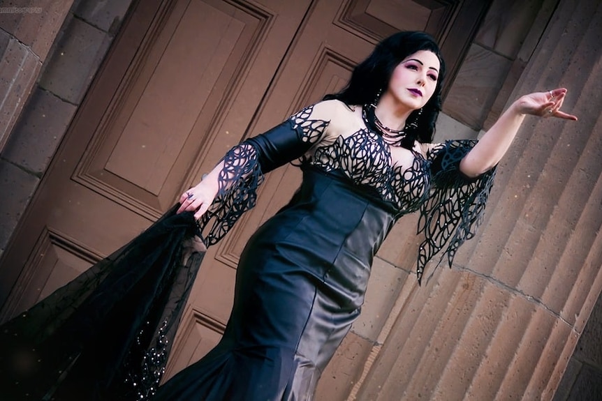 A woman in black, gothic attire and white make up poses for a photo.