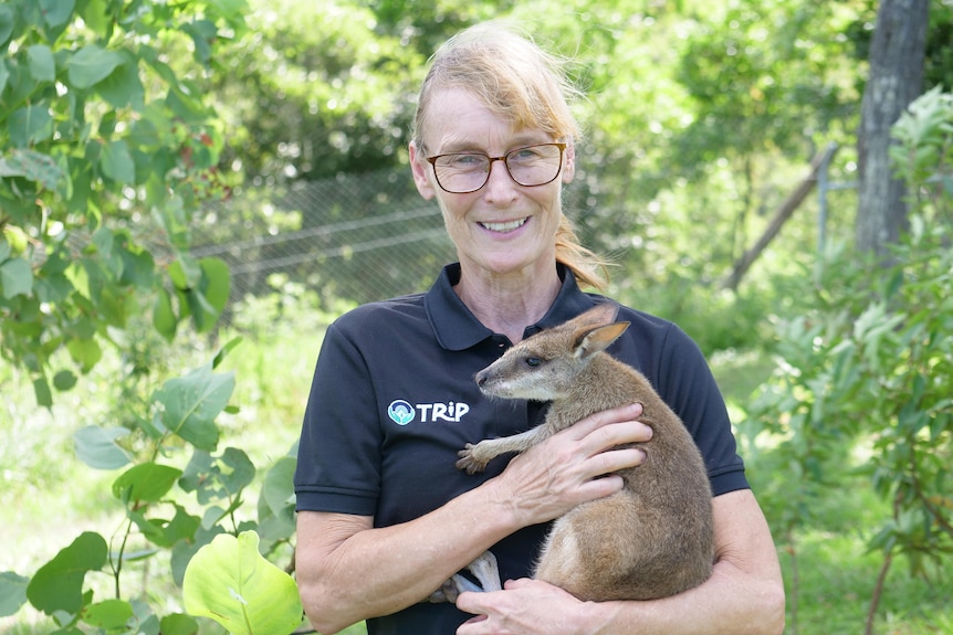 A woman holding a little wallaby, with greenery in the background
