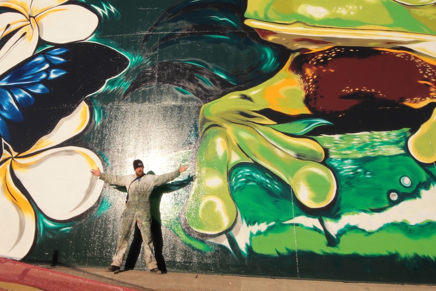 A large frog and butterfly painted on a tank with a man holding his arms outstretched.