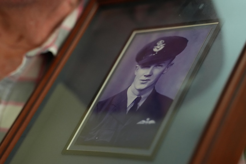 A close-up shot of an image in a wooden frame of a young man in an RAAF uniform, elderly man neck and shirt in view.