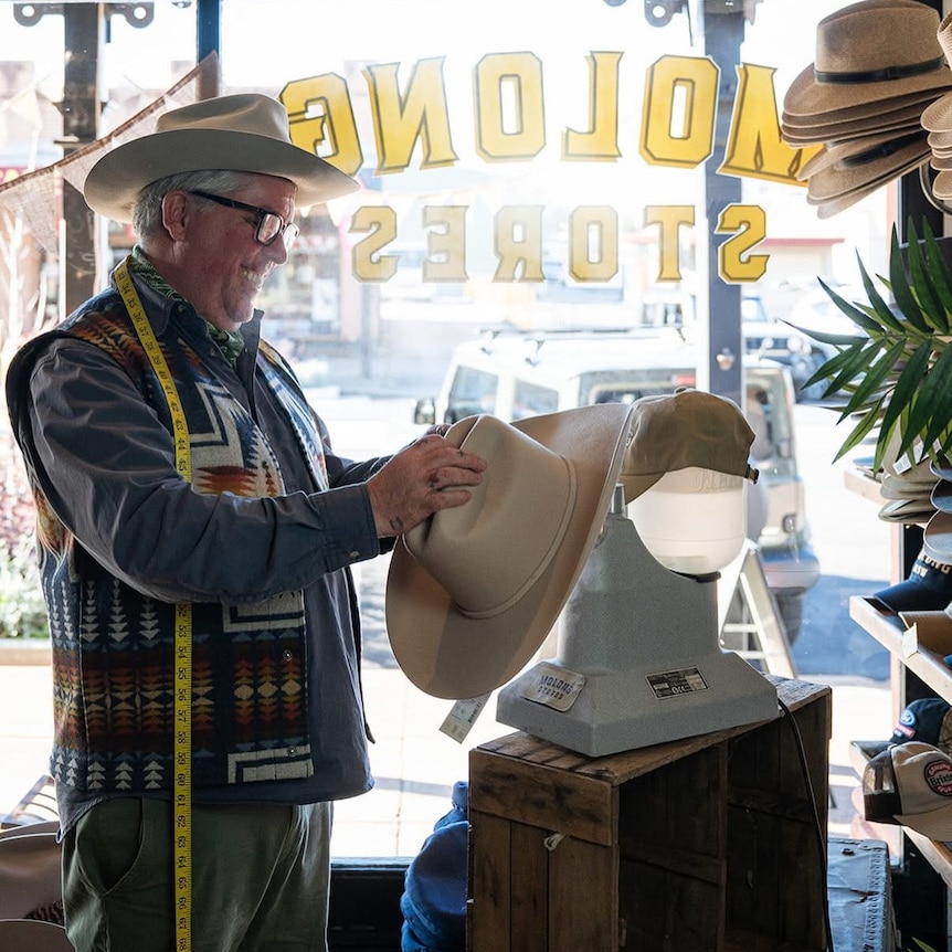 a man in a hat places a hat on a hat rack