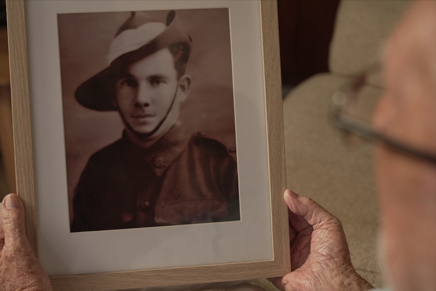 An elderly person's hands holding a framed sepia photograph of a man in an army uniform.