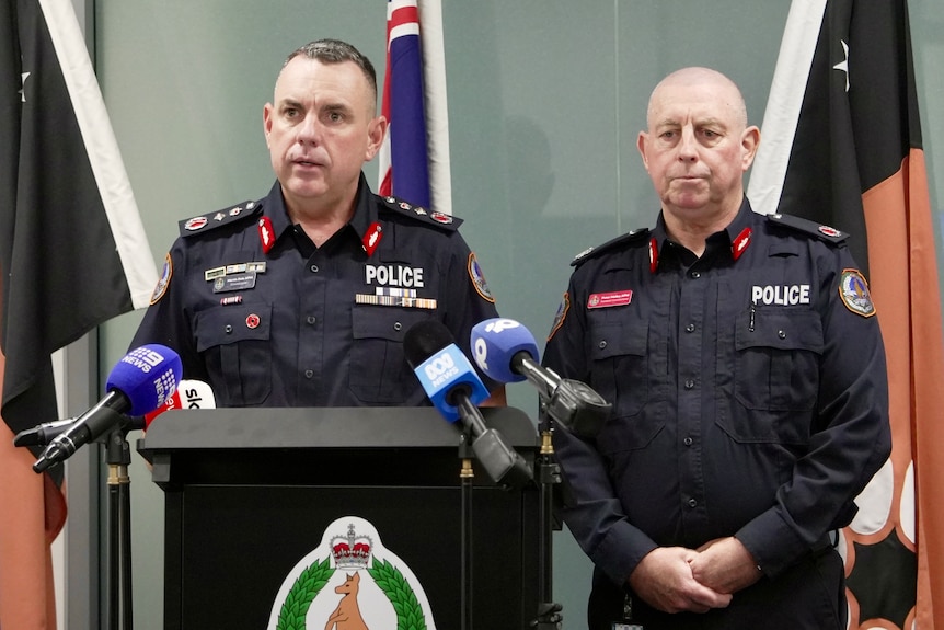 Two male police officers standing at a lectern and speaking into media microphones.