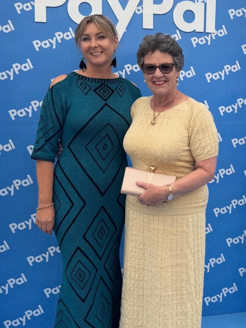 One middle aged woman wearing a long knitted blue dress standing next to an older woman wearing a knitted yellow dress 