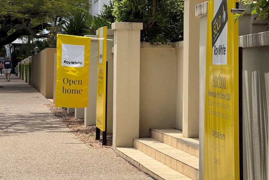 A yellow flag that says "open home" flying off a yellow real estate sign advertising an auction.