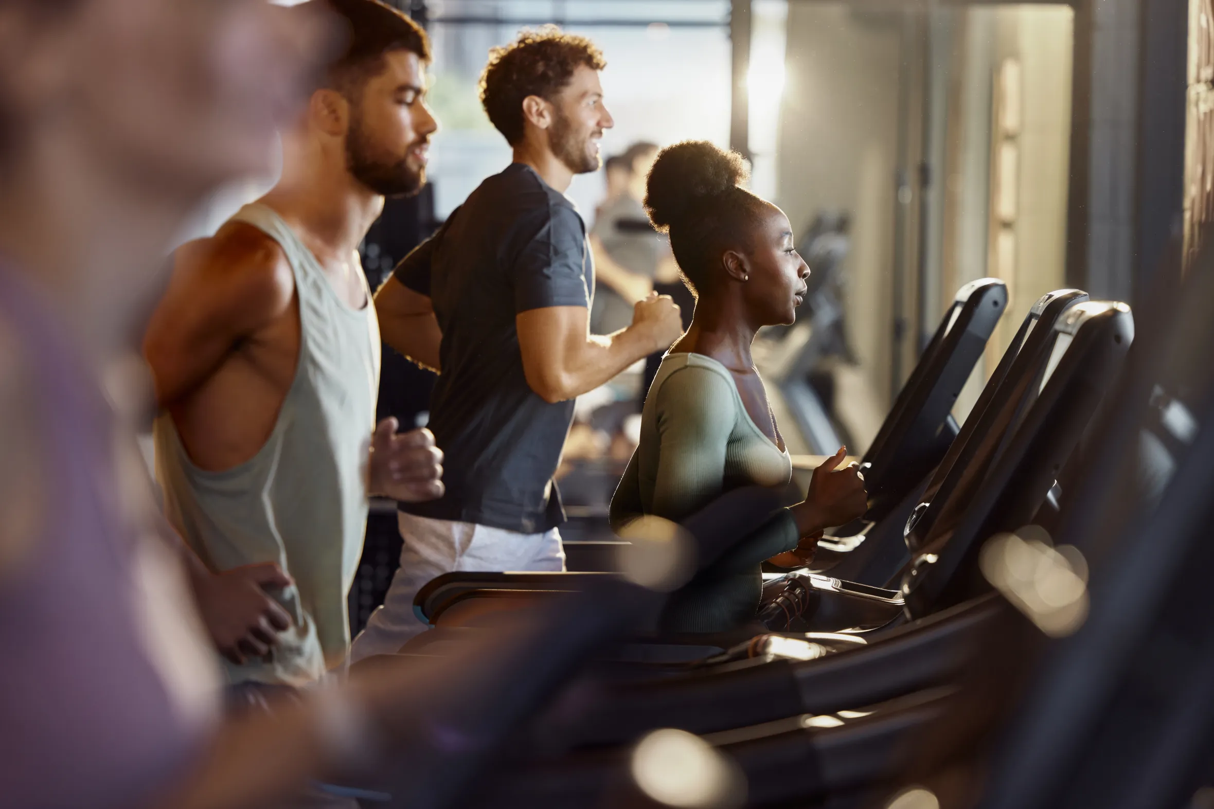 An African American woman exercising on a treadmill in a gym, with two men exercising on treadmills beside her.
