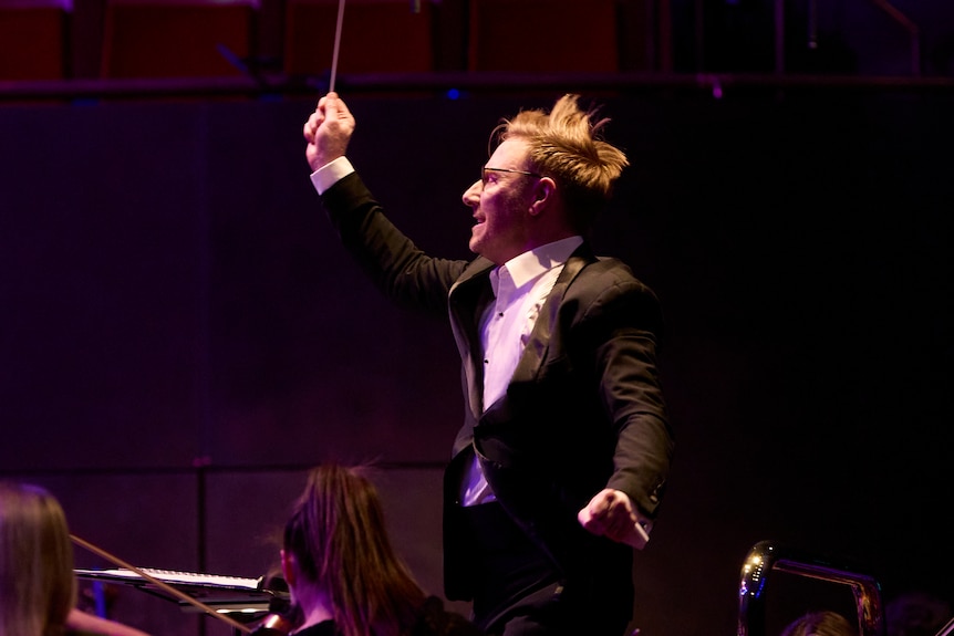 Benjamin Northey conducts the Melbourne Symphony in a tuxedo. His hair is flying in the air and his arms gesture dramatically.