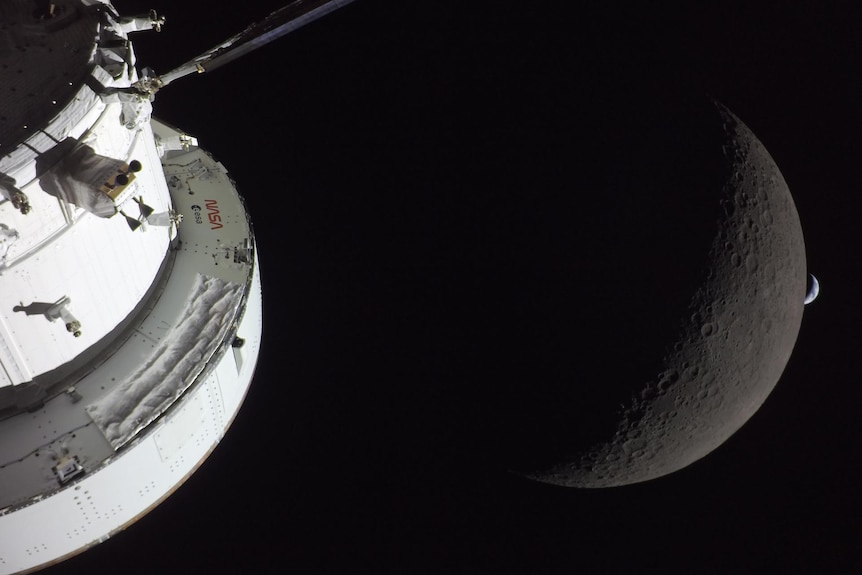 The right side of a spacecraft lit up by the Sun. A waxing crescent Moon is visible behind it. And then, a crescent Earth