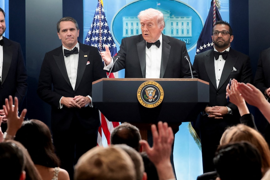 US President Donald Trump standing infront of a dais and answering questions from press.