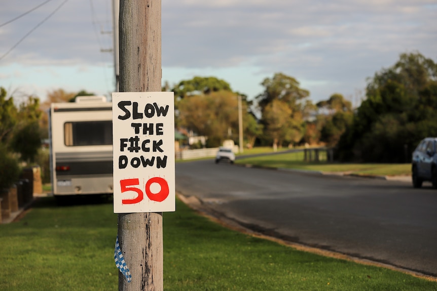 A road with a homemade sign affixed to a post that reads 'Slow the F#ck Down 50'