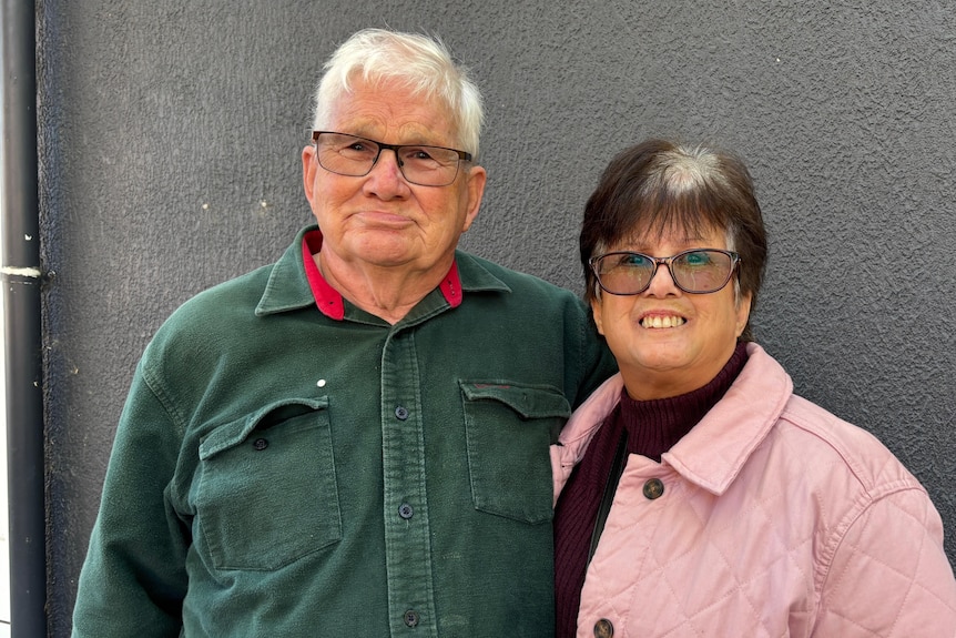 An older man in a green shirt and an older woman in a pink jacket smile at the camera.