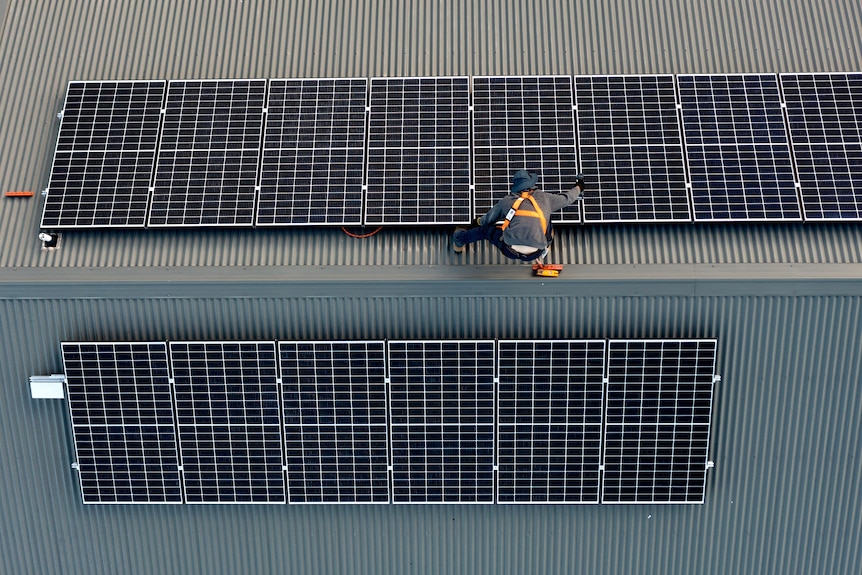 A worker installs solar panels on a rooftop.