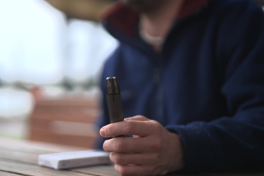 A person sitting at an outdoor table holds a prescription vape in their hand.