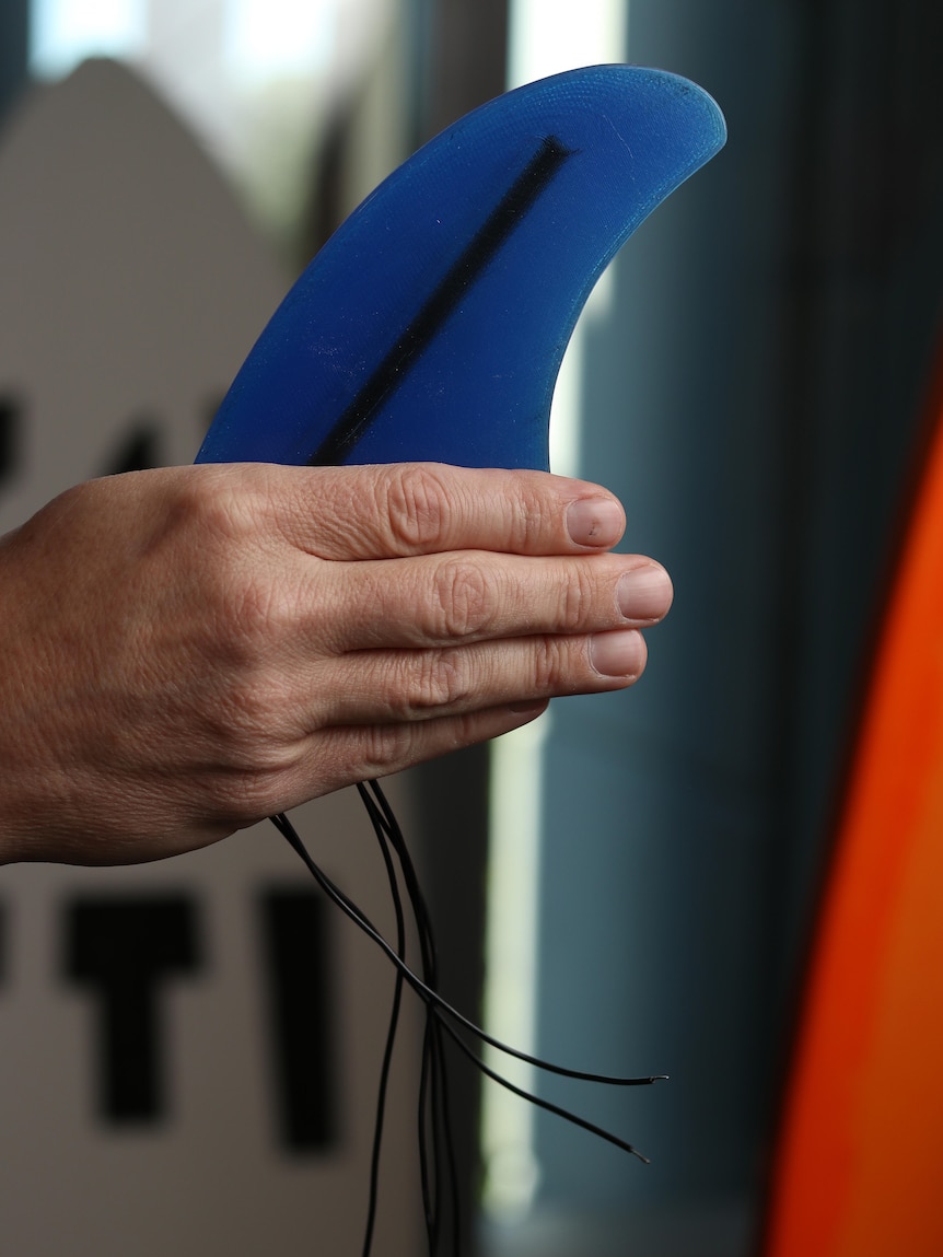 Hand holding blue surfboard fins with wires at the bottom