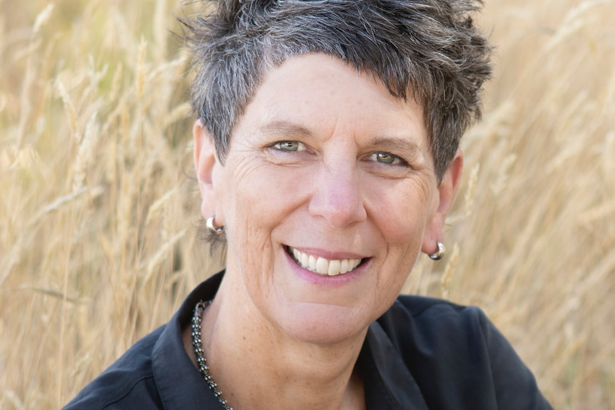 A close-up portrait of a smiling woman with salt-and-pepper cropped hair.