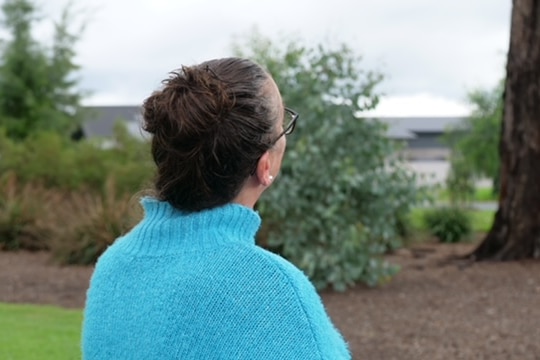 A woman with her back to the camera looking at a tree.