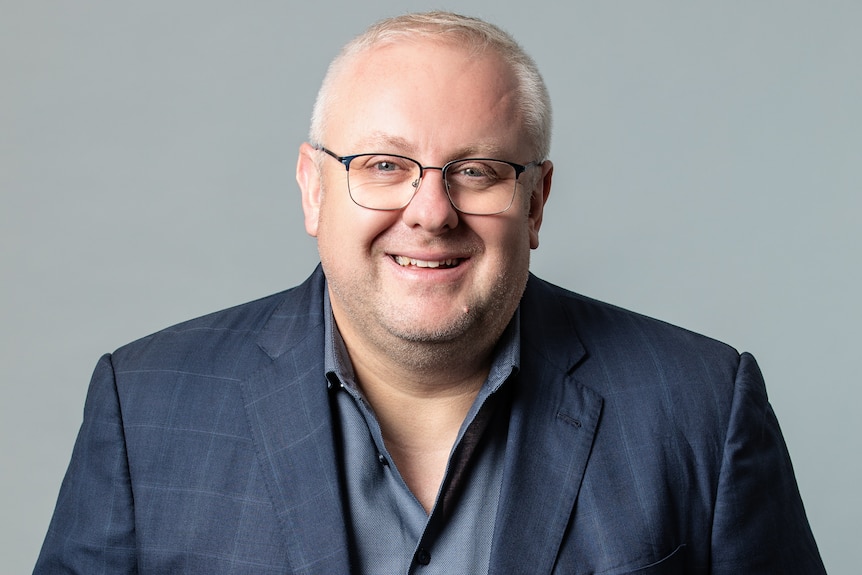 A profile image of a man with short, white hair, wearing glasses and a blue jacket.