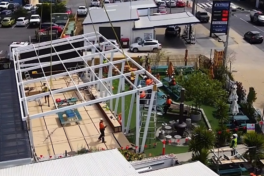 A roof is lowered towards a construction site.