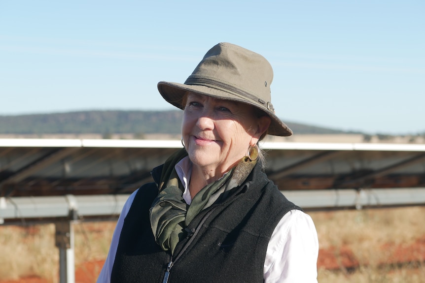 Gemma Purcell n front of solar panels, wearing a hat, smiling.
