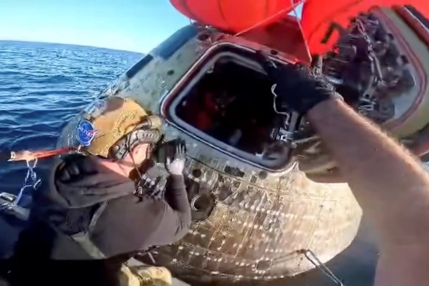 A member of the Navy recovery team, is seen opening the hatch to a space capsule floating in the ocean.