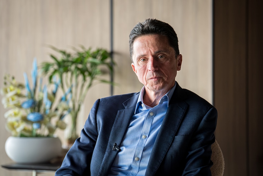 A middle-aged man looks seriously at the camera.