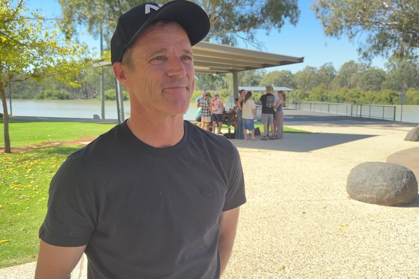 A man standing in a public park wearing a cap. 
