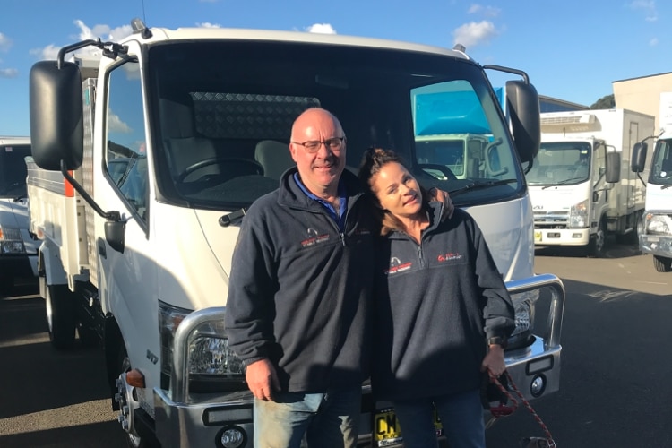 a man and a woman standing arm in arm in front of a truck