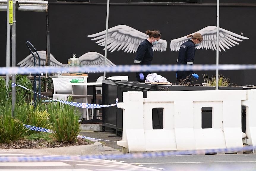 Two police officers walk past a mural of angel wings and they investigate the scene of a shooting