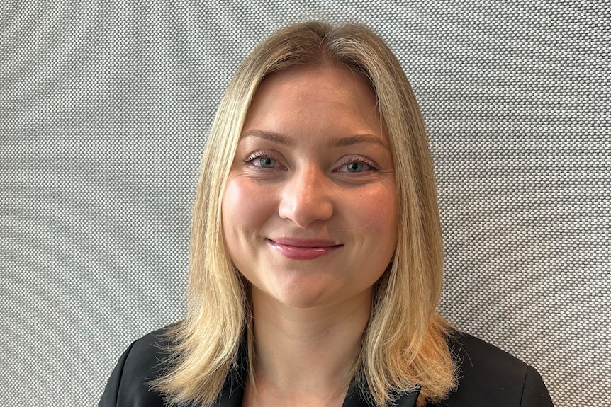 Madeline with blonde hair smiles at camera, wears dark suit, it's a headshot.