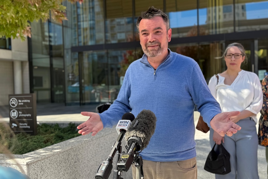 A man stands outside a court house speaking into a microphone.