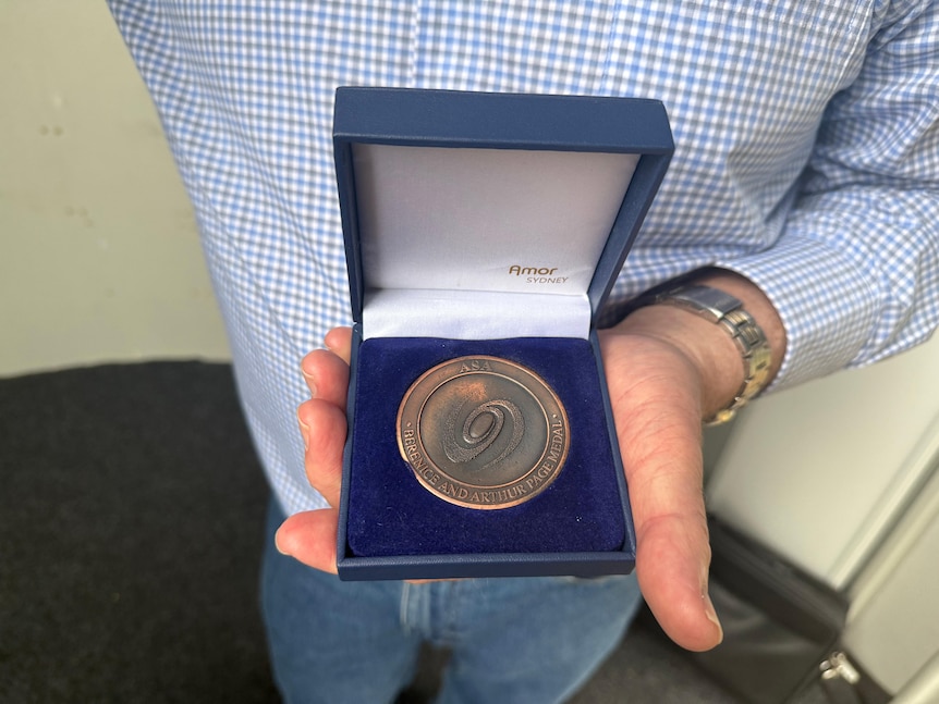 A blue box with a bronze-coloured medal sitting inside, held by a man