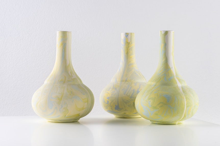 Three ceramic vases with round bottoms, painted with a yellow swirling pattern.