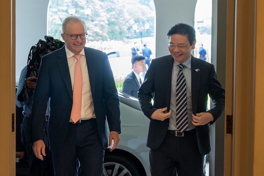 Twomen in suites walk through a door with bright sunlight behind them. 