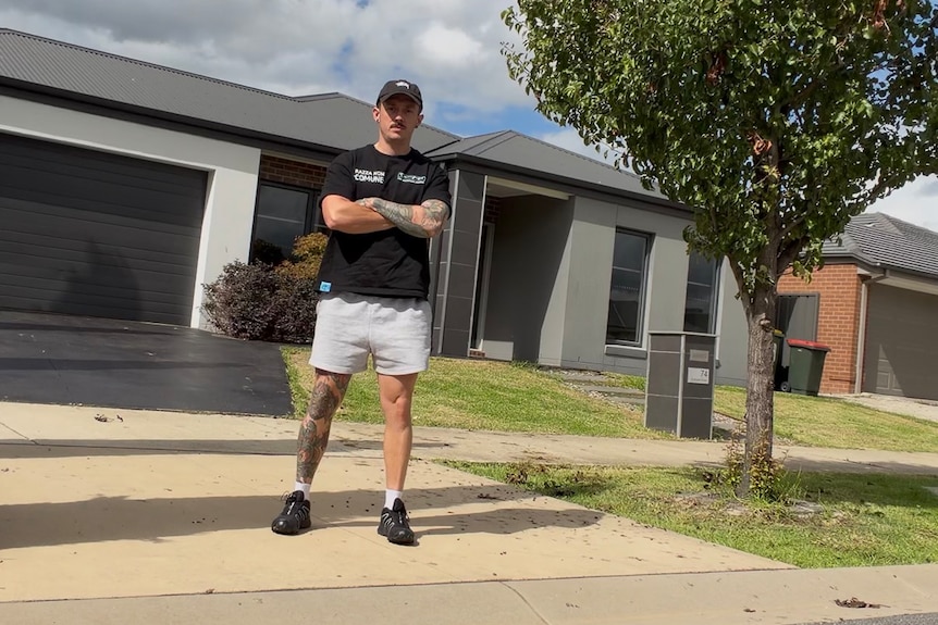 Man standing in front of house driveway with arms crossed.
