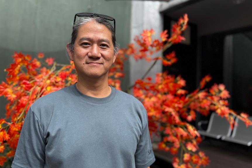 Man in a grey shirt with a pair of glasses on his head smiling to camera.
