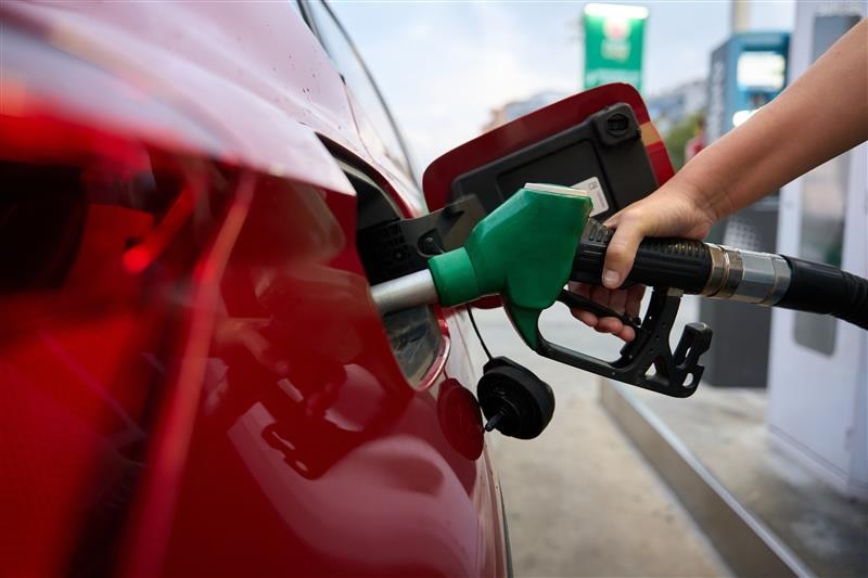 A hand inserts a petrol pump nozzle into a red car.