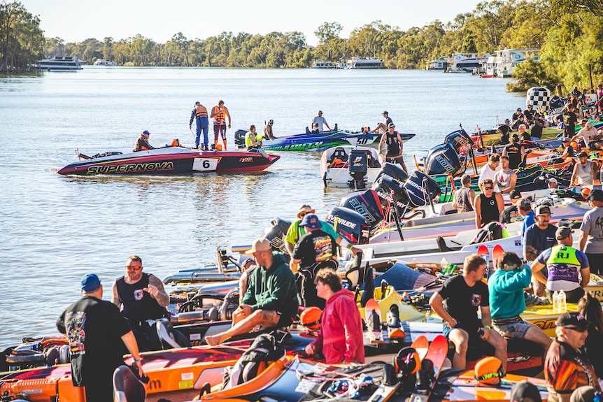 Dozens of people on water ski boats at a river bank, with the Murray River in the background.