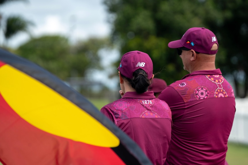 Two people wearing purple clothes and caps facing away from the camera