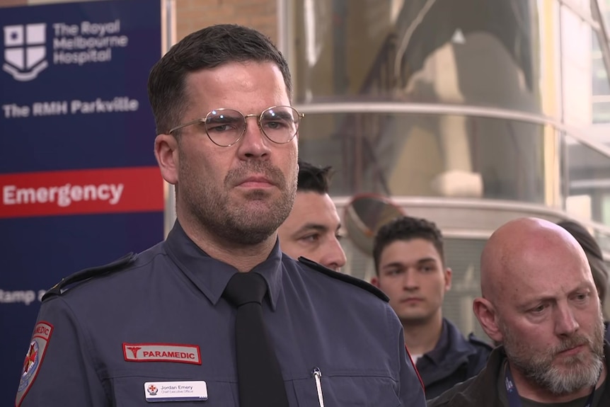 A tall man wearing a paramedics uniform and thin-rimmed glases