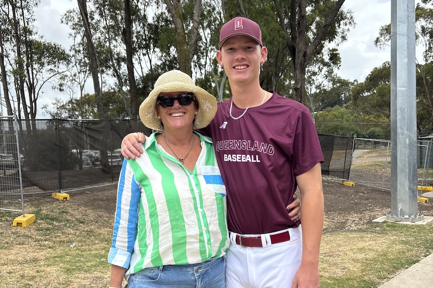 A young man in a maroon baseball outfit with his arm around a woman in a striped top and sun hat