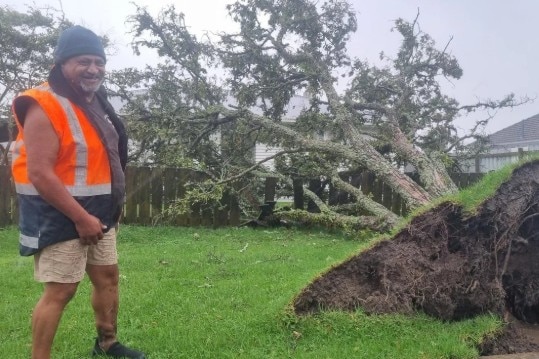 Man smiles wearing orange high-vis vest next to uprooted tree.