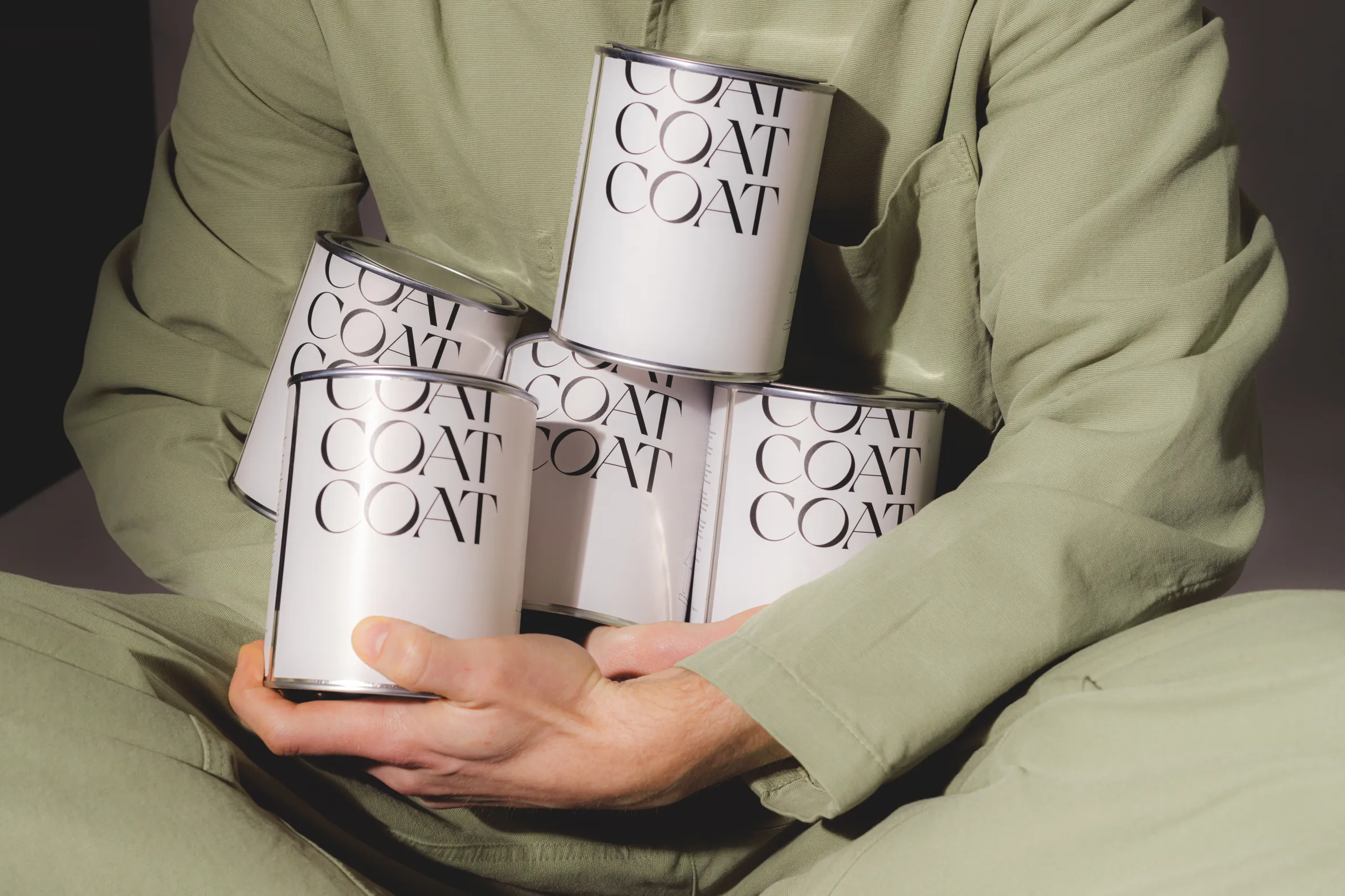 A person in green clothing holding several white paint cans labeled "COAT".