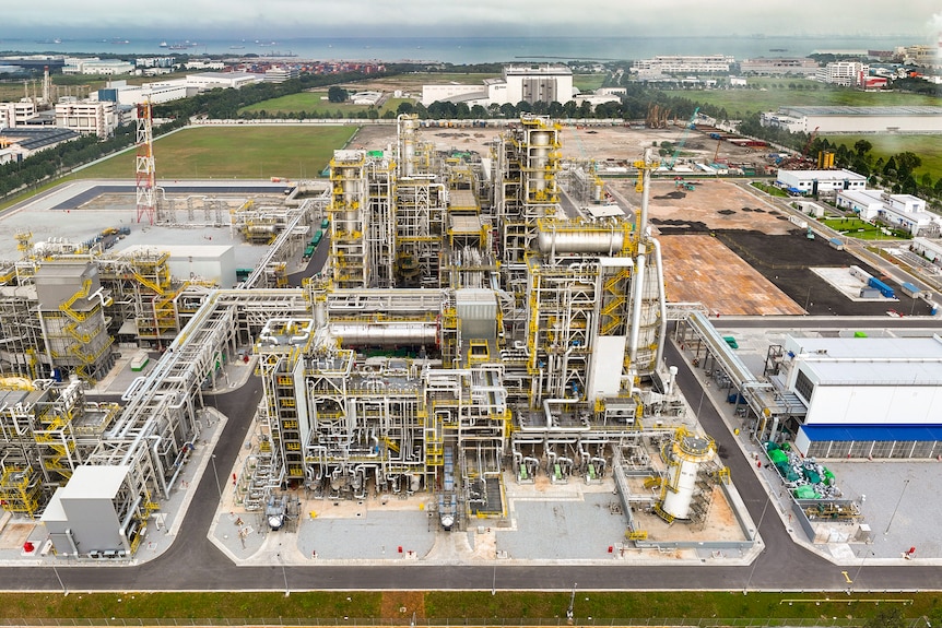 Large scale refinery with cooling towers and large industrial buildings with sprawling pipes span the foreground.