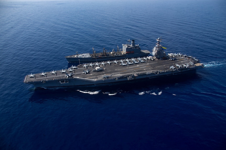 Overhead shot of a large aircraft carrier warship in the sea with fighter jets lining the deck.