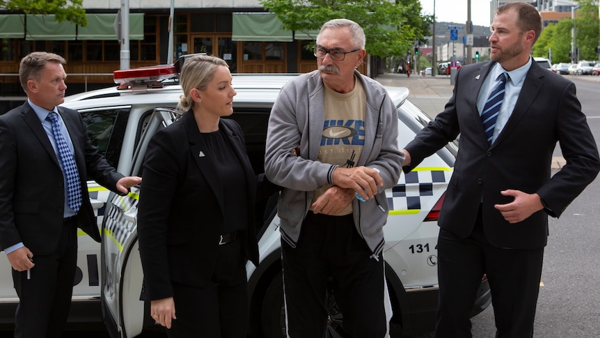 A man being led by police officers from a car.