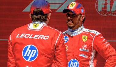 Hamilton facing Leclerc, who has his back to camera, in front of red and white FIA and F1 logo wall