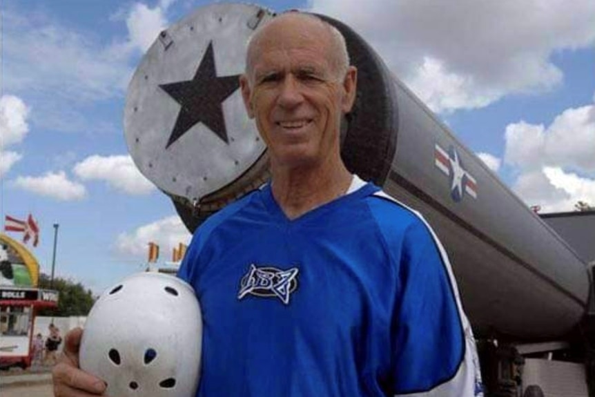 A man stands holding a helmet in front of a large cannon.