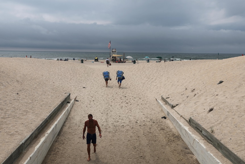 A wide shot of a sandy beach featuring an American flag on a pole, with the ocean in the background.