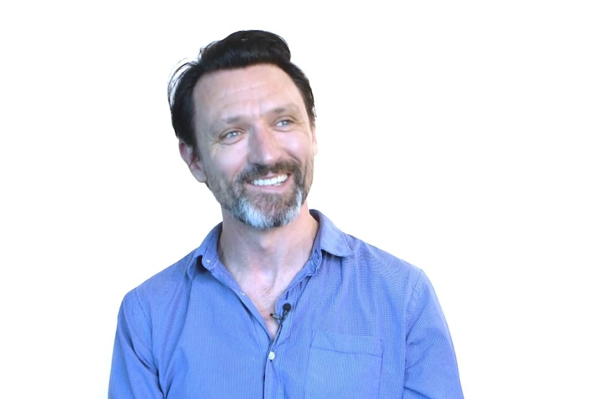 A smiling, dark-haired man in a button-up shirt.