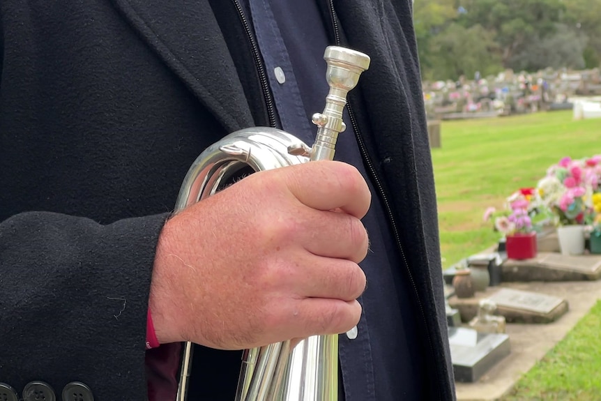 Hand holding a silver horn in front of a chest, with grave sites in the background. 